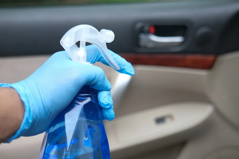 Blue gloved hand spraying cleaner on a car door panel interior