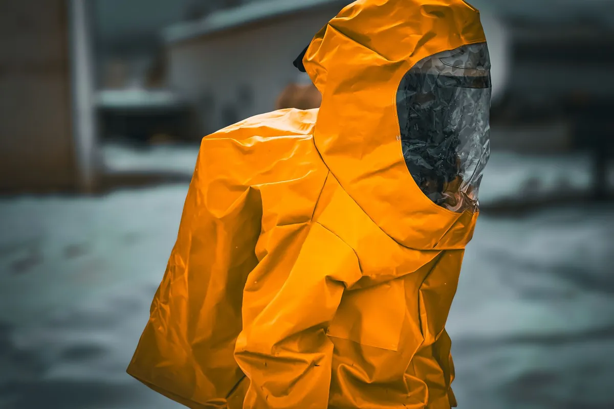 Worker in a hooded orange protective suit with a dark visor standing outdoors